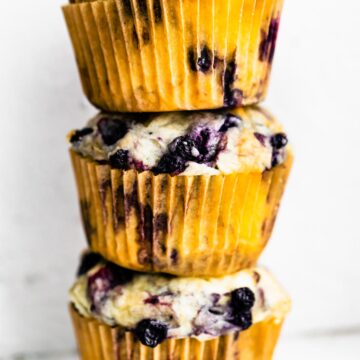A stack of 3 gluten free blueberry muffins in muffin liners on top of each other.