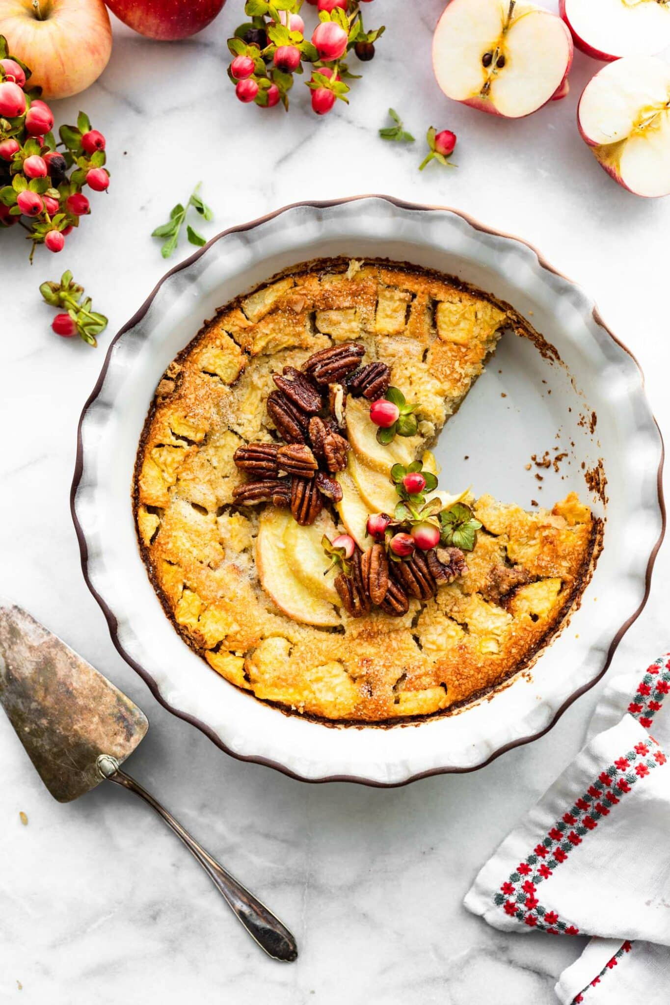 Gluten free apple pie in a white pie pan with a slice taken out topped with sliced apples and whole pecans