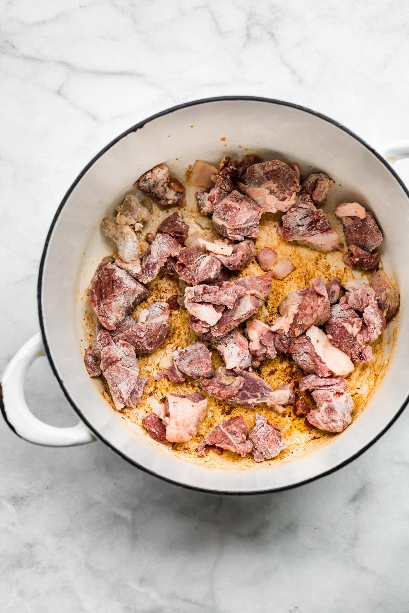 Overhead photo of lamb stew meat coated in flour in a white soup pot.