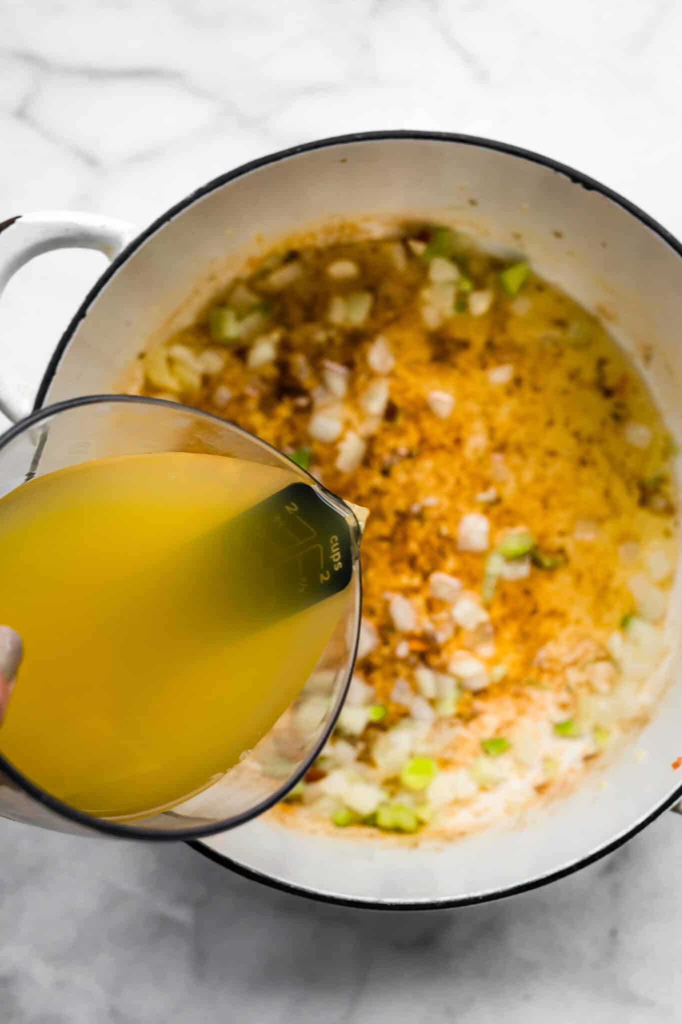 Broth being poured into a a soup pot of sauteed vegetables.