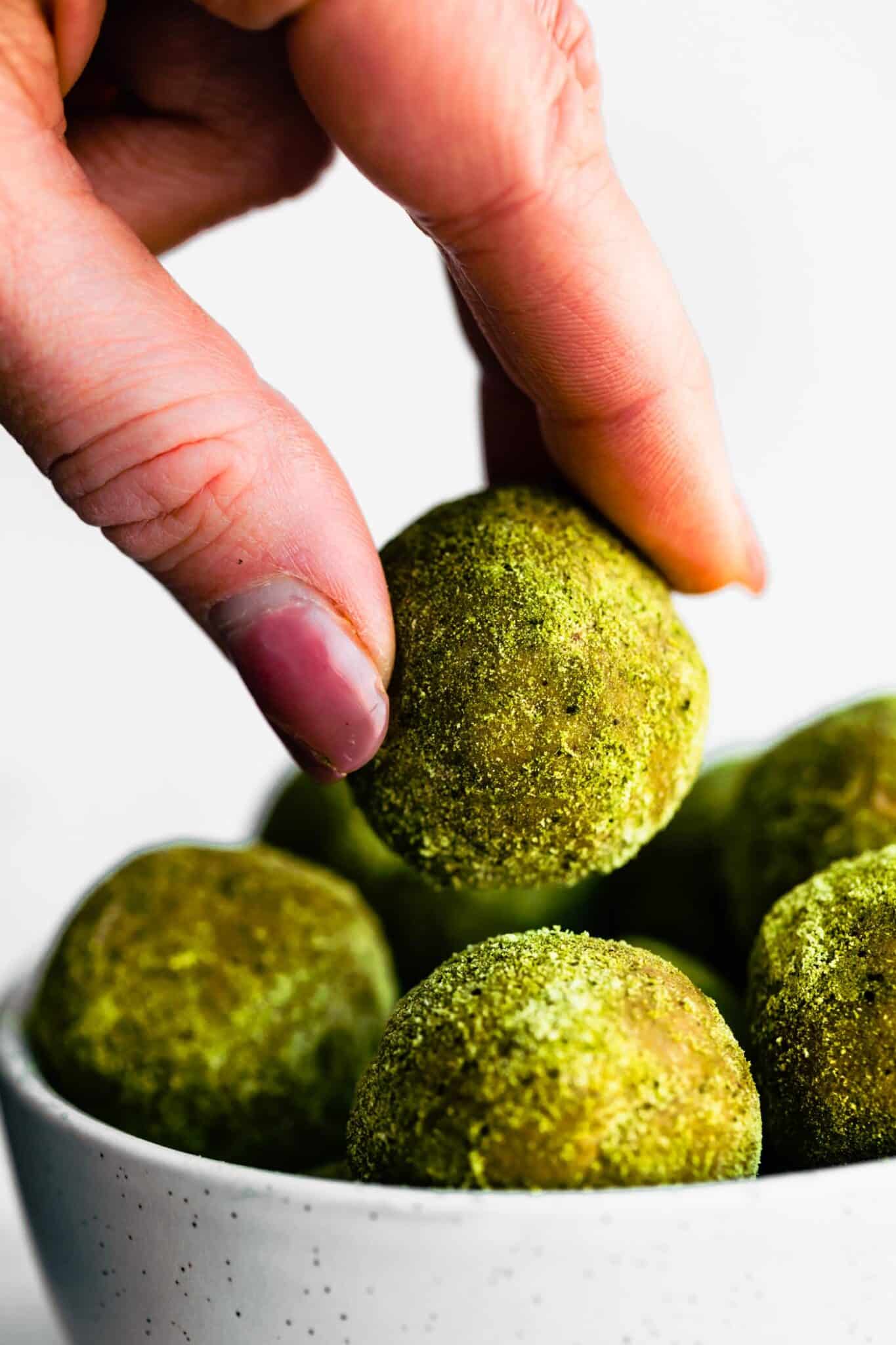 woman's hand picking up a green matcha protein bite from bowl