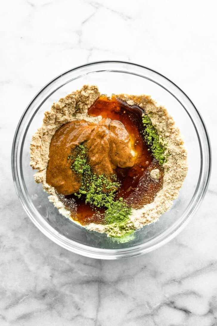 ingredients to make matcha protein bites in a clear bowl, not mixed.