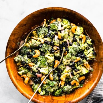 A creamy no mayo broccoli salad in a wooden bowl with two spoons.