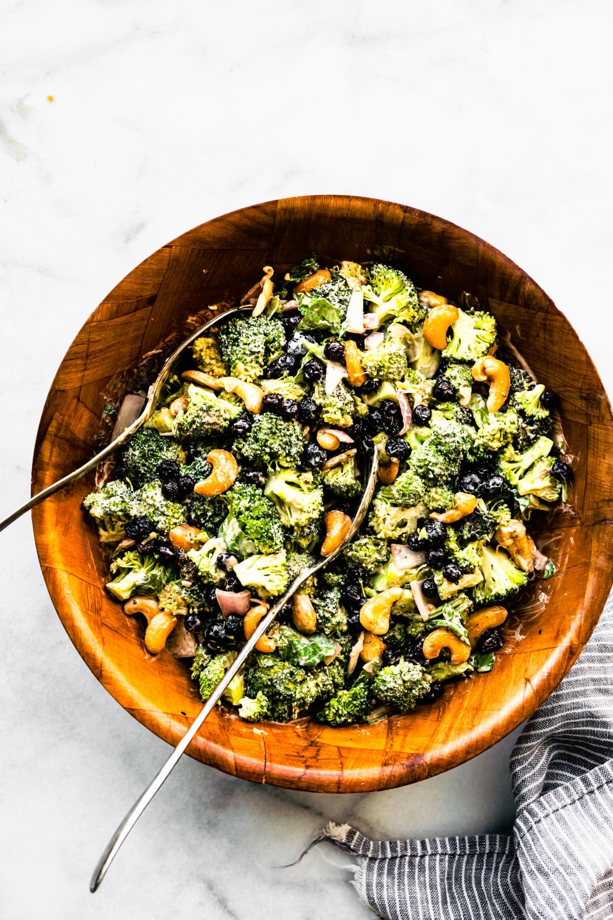 A creamy no mayo broccoli salad in a wooden bowl with two spoons.