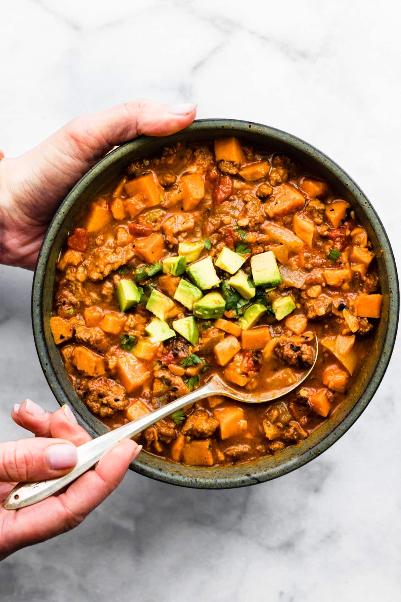 A woman's hands holding a bowl of chipotle sweet potato chili and a spoon.