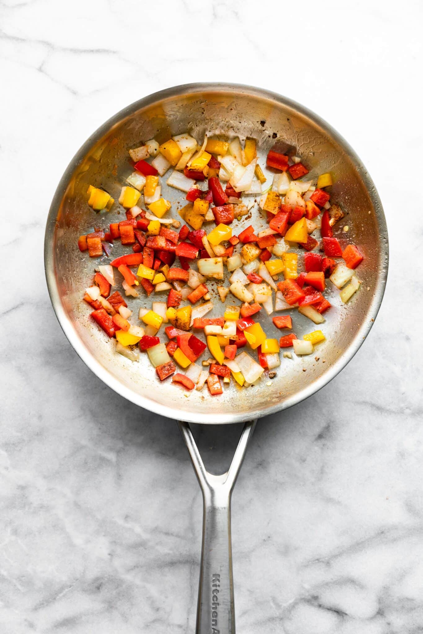 Sauteed onions and bell peppers in a metal saute pan.