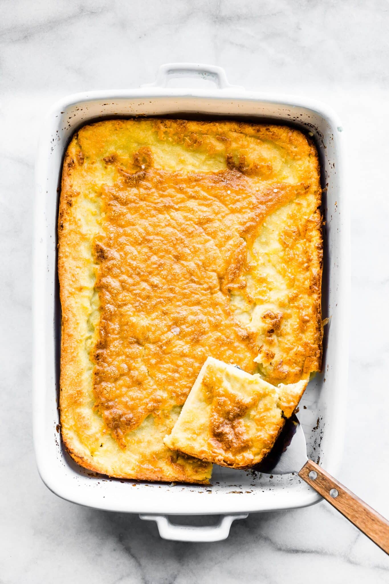 Overhead photo of an oven baked pancake with a spatula removing a slice.