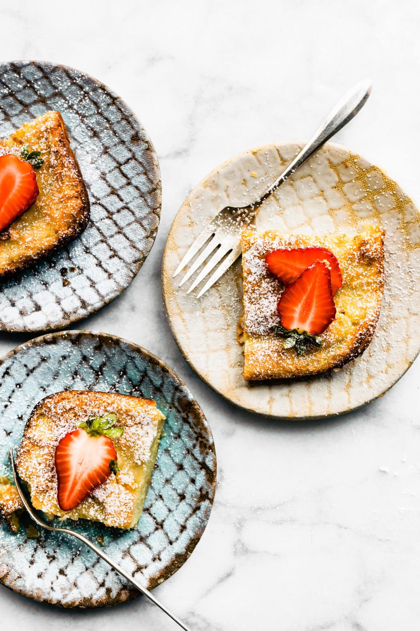 Three plates each with a slice of Swedish Pancakes topped with strawberries and powdered sugar.
