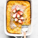 A gluten free Swedish Pancake topped with sliced strawberries and a slice removed.