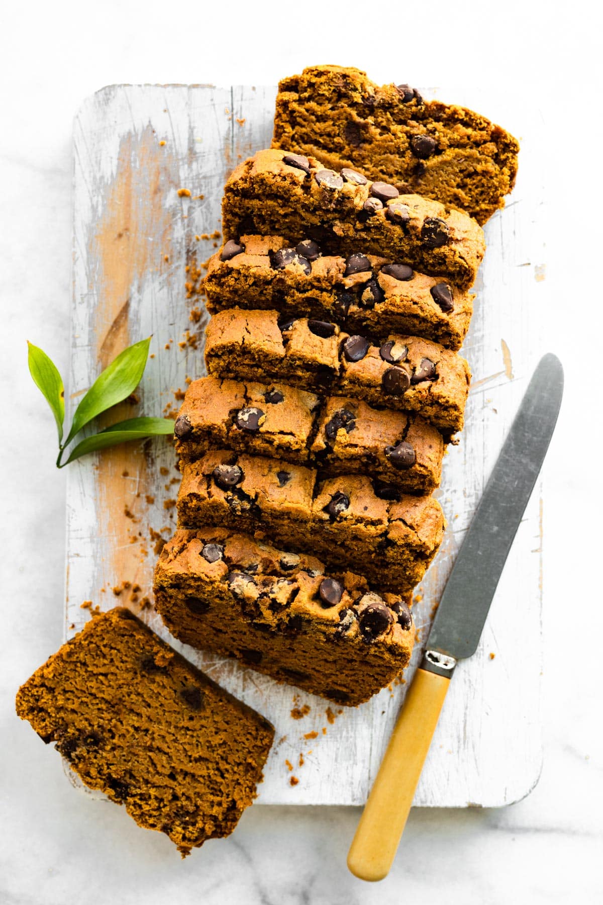 Overhead photo of sliced vegan pumpkin bread on a white wooden cutting board.