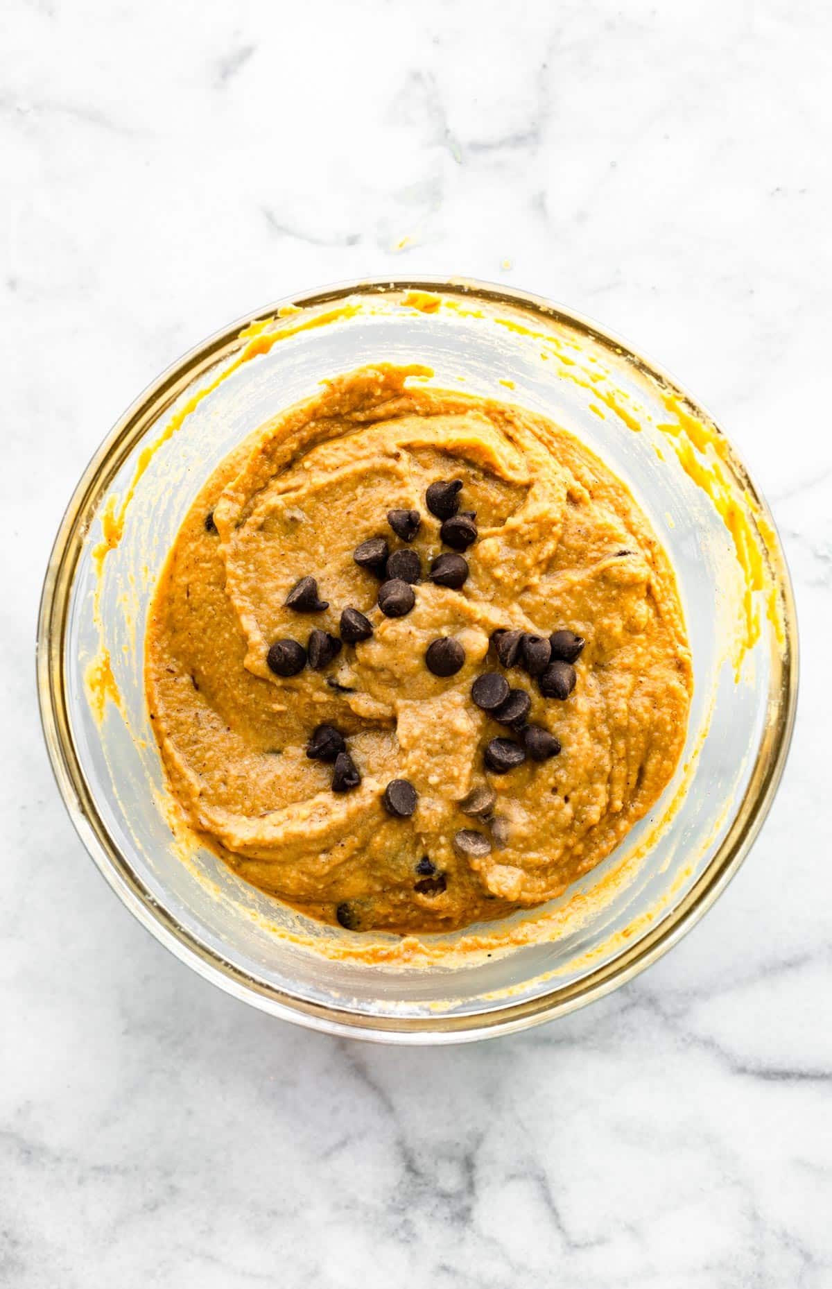 A clear glass bowl with pumpkin bread batter with dark chocolate chips.