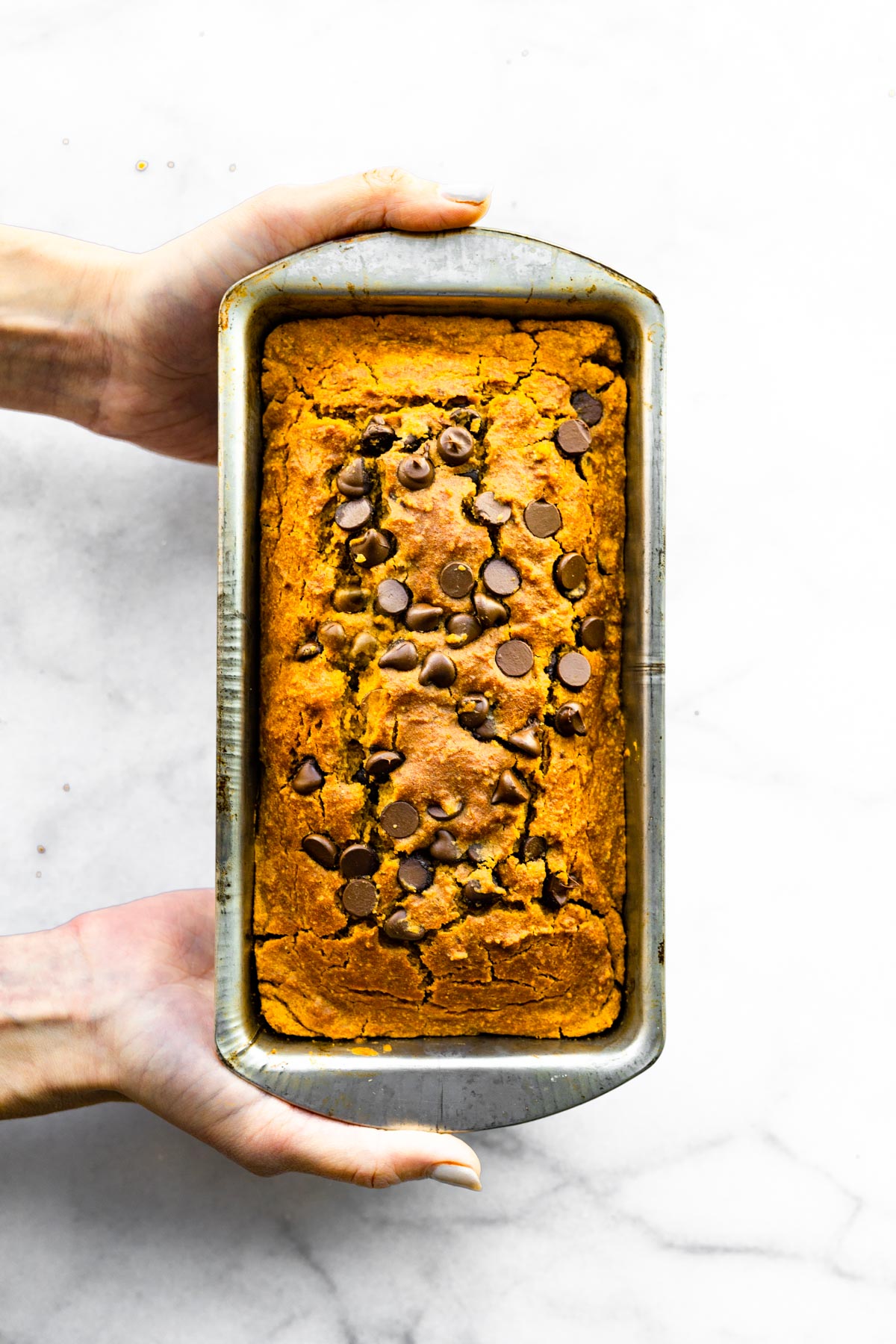 Two woman's hands holding a loaf of gluten free pumpkin bread in a metal pan.