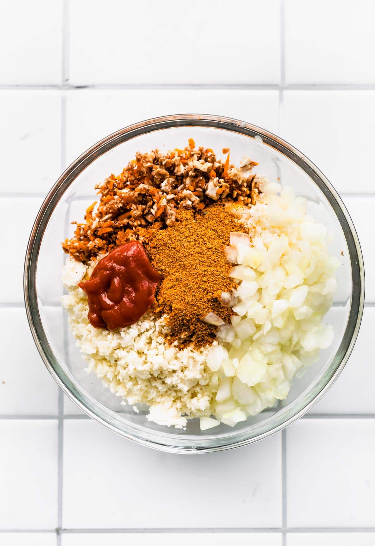 Diced onions, riced cauliflower and spices in a glass bowl for vegan taco meat.