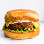 A vegan black bean burger with a bun, melted cheese, chipotle mayo and lettuce.