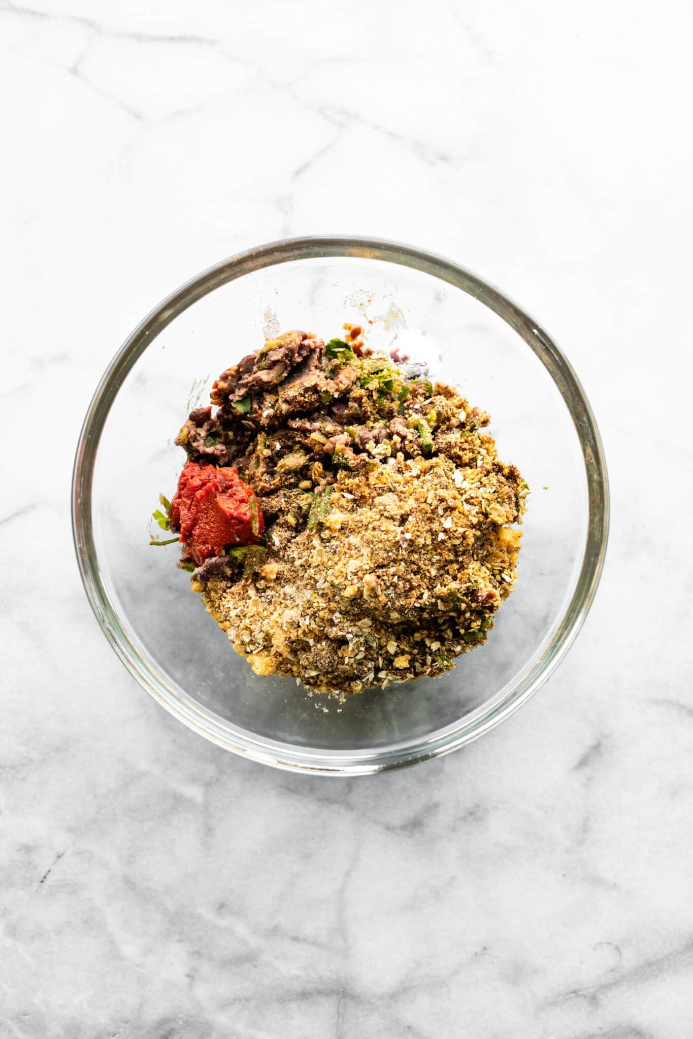 Gluten free panko on top of black beans and tomato paste in a glass mixing bowl.