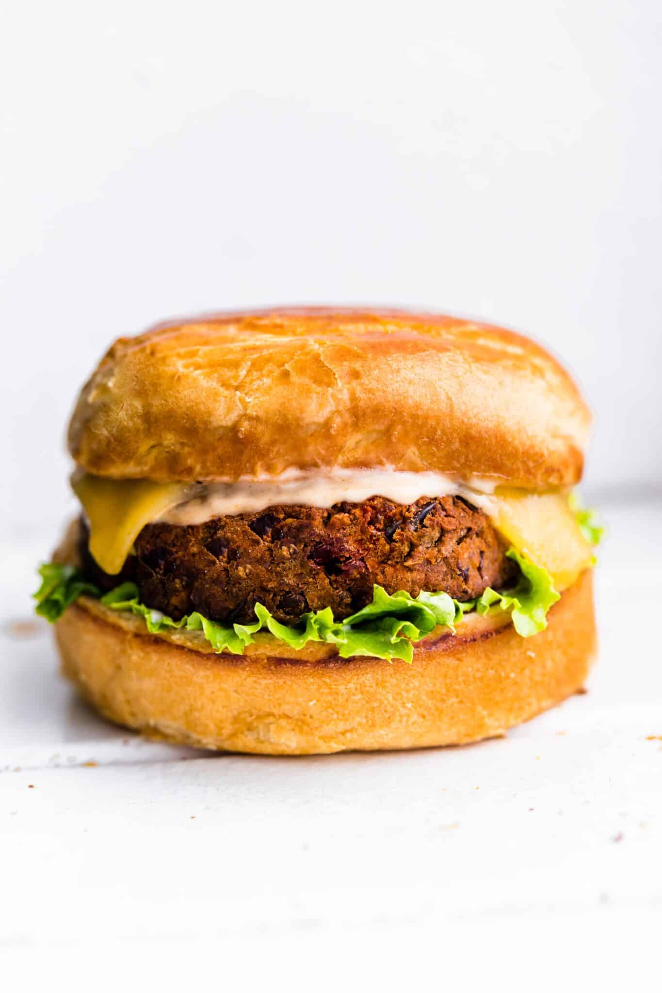 A vegan black bean burger with a bun, melted cheese, chipotle mayo and lettuce.