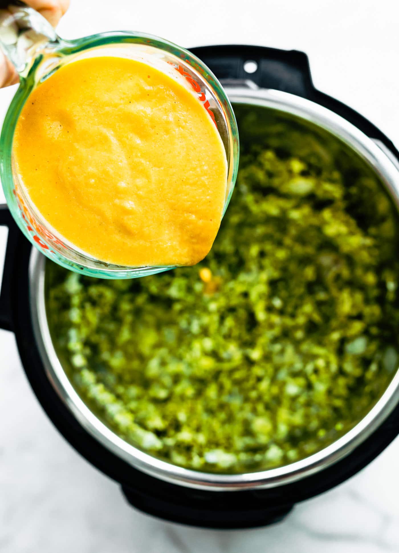 Chopped broccoli florets in an instant pot with someone pouring cheese sauce on top.