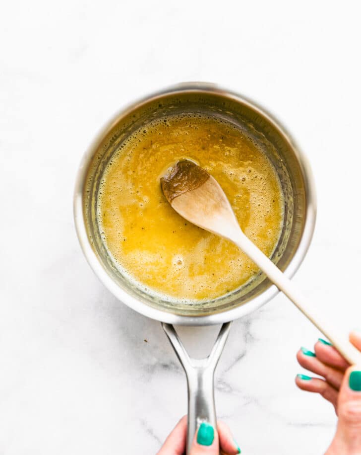 Wooden spoon stirring cheese sauce ingredients in a pot.