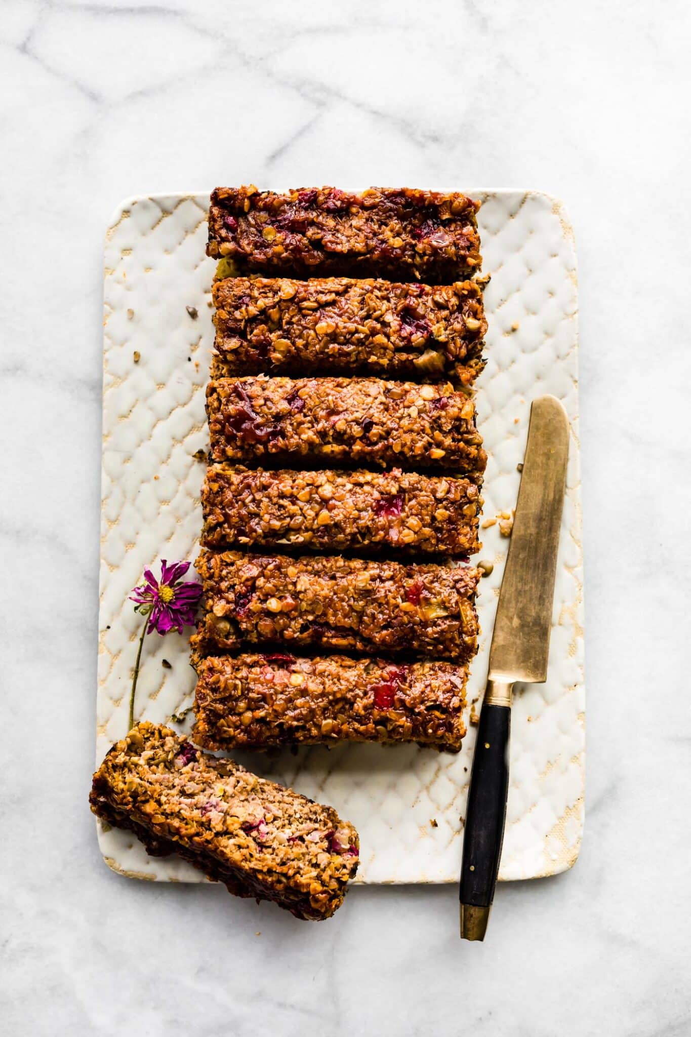 Overhead photo of a baked lentil loaf sliced on a white plate with knife on the side