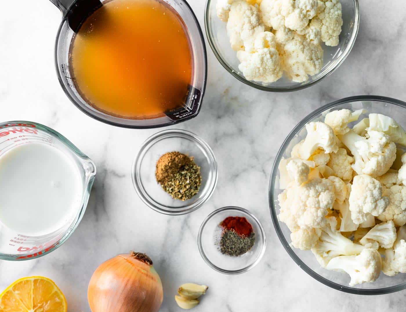 overhead photo of ingredients for cauliflower soup. Broth, coconut milk, onion, spices, and cauliflower